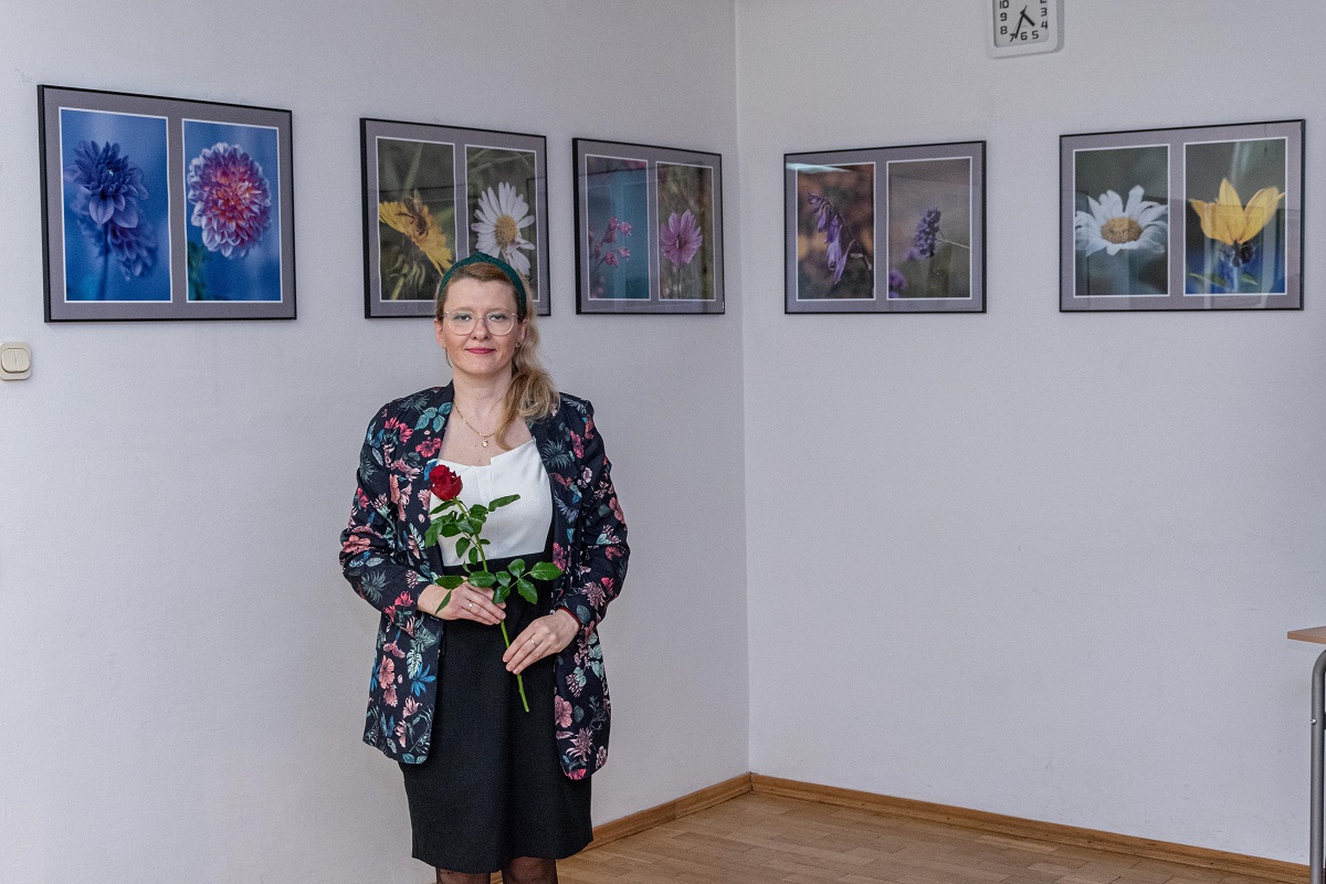 Autorka jednej z wystaw fotograficznych stojąca na tle swoich zdjęć. W rękach trzyma czerwoną różę.