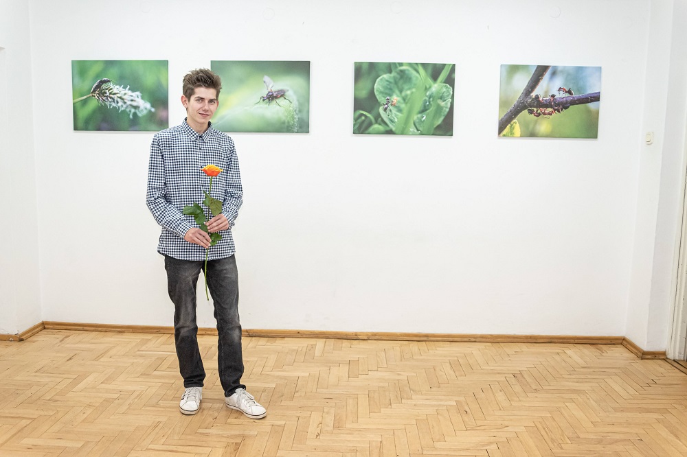Słuchacz Studium Przemysław Bielański stojący na tle swojej wystawy fotograficznej