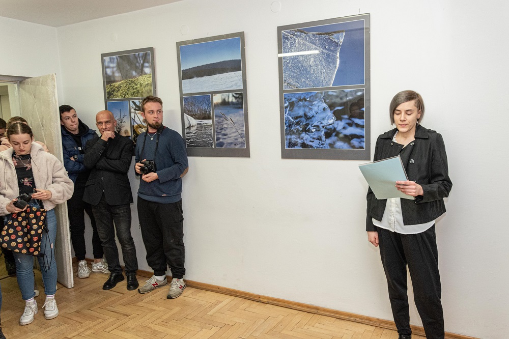 Na zdjęciu autorka wystawy fotograficznej  Małgorzaty Truś stojąca na tle swoich zdjęć, które przedstawiają motywy zimowe. 