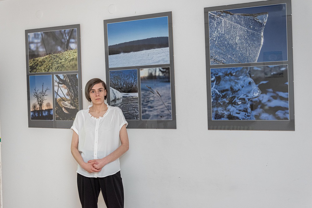 Na zdjęciu autorka wystawy fotograficznej  Małgorzaty Truś stojąca na tle swoich zdjęć, które przedstawiają motywy zimowe. 
